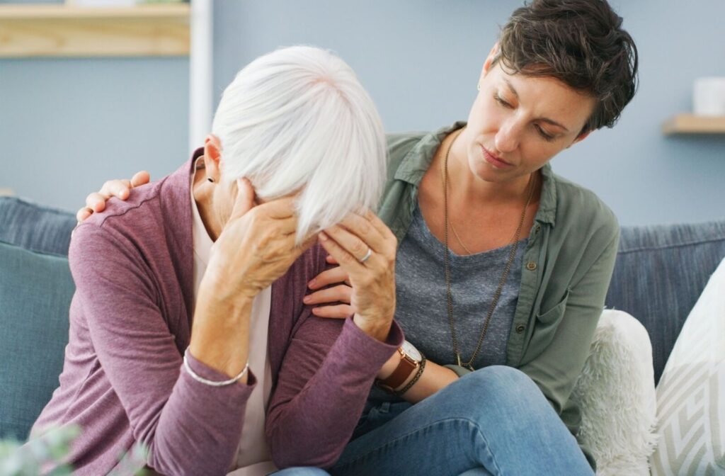 An adult child comforts their older parent on the couch during an emotional conversation