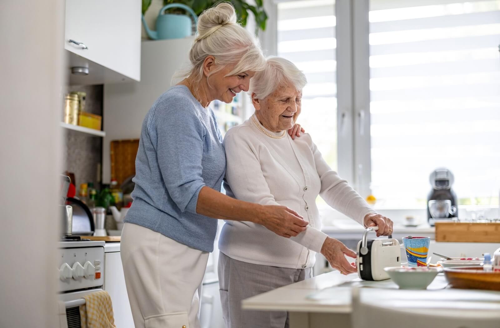 An adult child helps their older parent with a small handheld radio in their kitchen in a memory care community