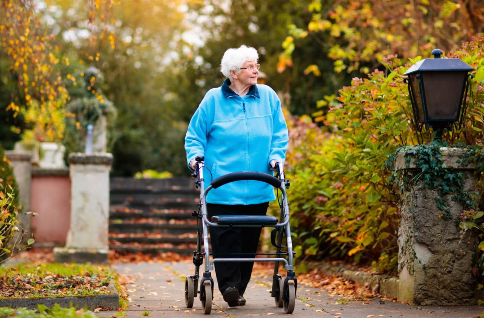 A mature person experiencing Parkinson's disease walking outside with supportive footwear and a walker.