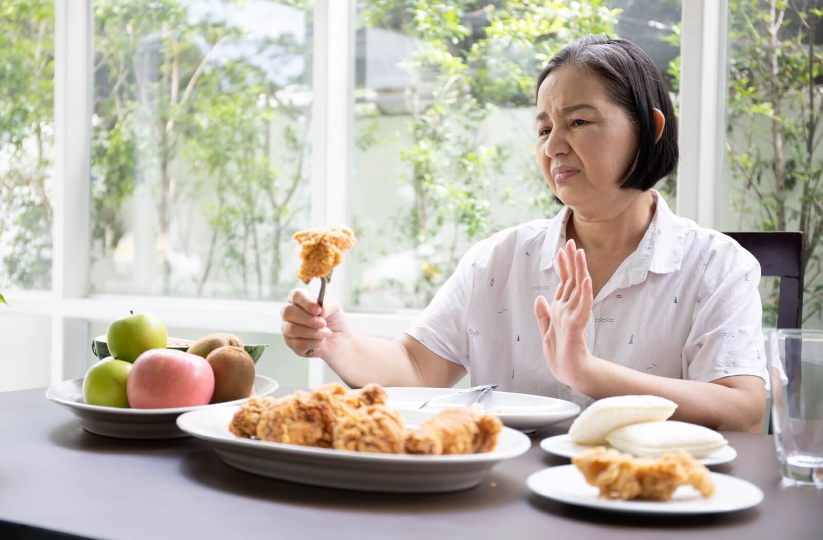 Older adult rejecting fried chicken, surrounded by unhealthy fried foods, with fresh fruit nearby, hinting at brain health