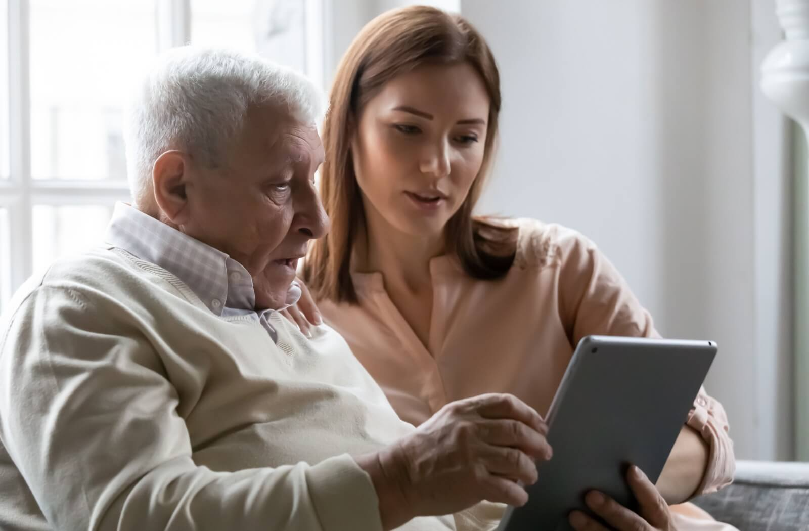 A caring adult looks at memory care communities with their senior parent, pointing at the screen.
