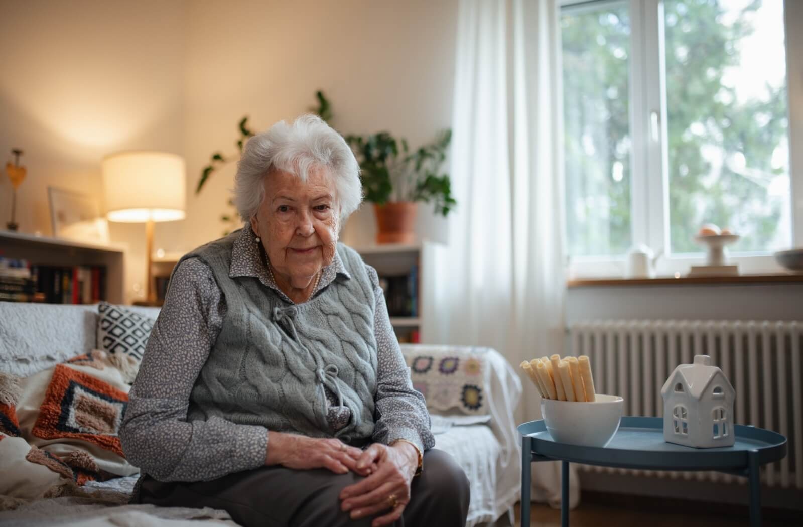 An older adult smiles while sitting on a couch in a well-decorated living room in their home in memory care